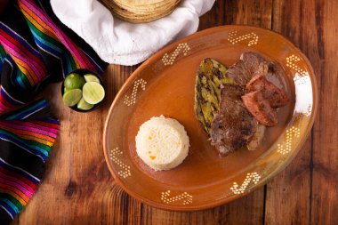 Kızarmış et, nopal kaktüs ve sucuk adı verilen sucuklu domuz sosisi yanında da tipik bir Meksika kil tabağında servis edilen beyaz pirinç..