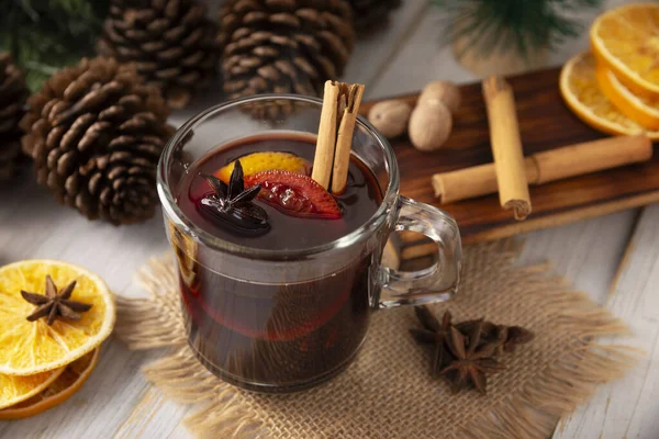 Spiced wine or Christmas mulled wine with orange, cinnamon, star anise, clove, nutmeg and other ingredients on a wooden rustic table. Traditional hot drink at winter time and Christmas holidays.