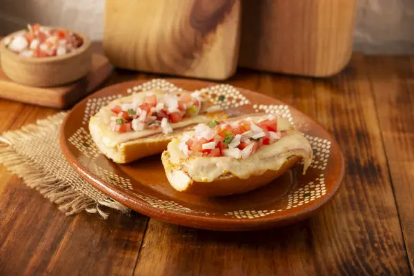 stock image Molletes. Mexican recipe based on bolillo bread split lengthwise, spread with refried beans and gratin cheese, adding pico de gallo sauce and some protein such as ham, bacon or chorizo.