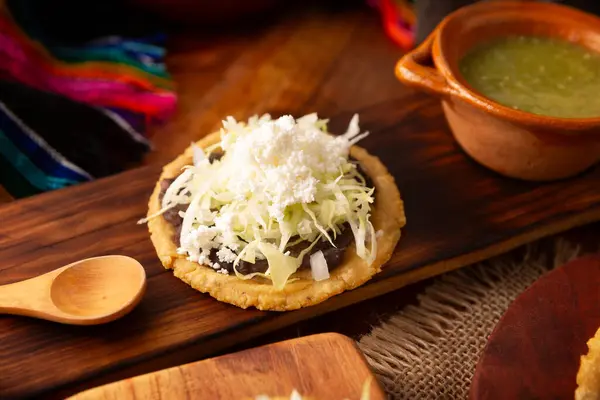 stock image Sope. Traditional homemade Mexican food prepared with flattened and pinched on the border fried corn dough covered with refried beans, green or red sauce, lettuce, cheese, onion and sour cream.