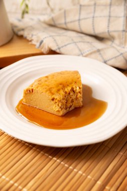 homemade flan dessert, also known as creme caramel, caramel custard pudding or egg custard, served on white plate on wooden table.