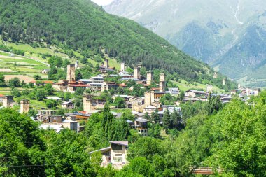 Mestia şehrinin manzarası. Ortaçağ savunma taş kuleleri, yasal boşluklar, konut evleri. Ağaçlar, tepeler çalılarla ve ağaçlarla kaplı..