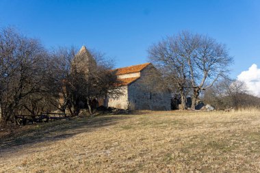 Alvani köyünün Baptist Bazilikası ve çan kulesi. Etrafta yapraksız ağaçlar. Parlak gökyüzü.
