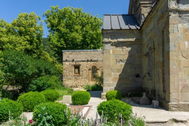 Manastırın iç avlusunda. Kilisenin taş duvarı, yontulmuş çalılar, ağaçlar ve çiçekler. Martkopi manastırı, Georgi.