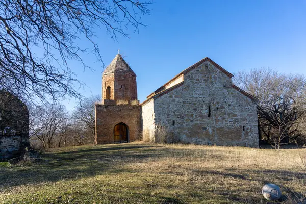 Stock image Faded grass on the hill and St. John the Baptist basilica of Alvani village and bell tower.