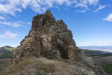 Kojori kalesinin taş ve tuğla duvarları. Parlak mavi gökyüzü ve bulutlar. Dağlar, köyler ve vadiler görünür.