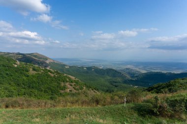 Kayaların ve dağların manzarası. Parlak mavi gökyüzü ve bulutlar. Ön planda yeşil çimenler var. Yakınlardaki dağların ve köylerin manzarası. Georgia