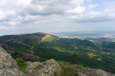 Kayaların ve dağların manzarası. Parlak mavi gökyüzü ve bulutlar. Ön planda yeşil çimenler var. Yakınlardaki dağların ve köylerin manzarası. Georgia.