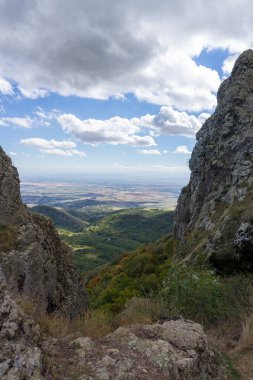 Kojori kalesinin harabelerinden kayaların arasından manzara manzarası. Parlak mavi gökyüzü ve bulutlar. Dağlar, kayalar, vadideki köyler ve ufuktaki bulutlar. Renkli çalılar ve yeşil çimenler