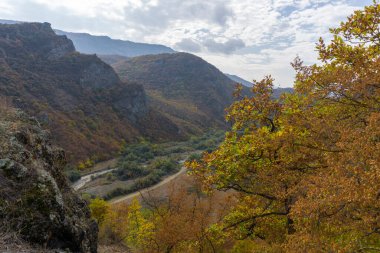 Dağları, nehri, tarlaları ve tepeden vadiyi görüyorum. Sonbahar renkleri kırmızı, sarı, yeşil ve turuncu yapraklar ve çalılar. Açık mavi gökyüzü ve bulutlar. Tepeler ve tepeler