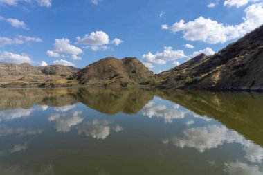 Göl ve dağların güzel manzarası. Parlak mavi gökyüzü. Bulutlar suya yansıyor. Kuru ot. Georgia 'daki Mravaltskaro Barajı.