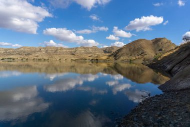 Göl ve dağların güzel manzarası. Parlak mavi gökyüzü. Bulutlar suya yansıyor. Kuru ot. Georgia 'daki Mravaltskaro Barajı.