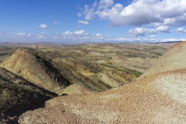 Georgia 'daki Mravaltskaro Barajı yakınlarında çok renkli dağlar. Kayaların yüzeyinde gri, yeşil, kırmızı ve turuncu toprak şeritleri. Bulutlu parlak mavi gökyüzü. Kuru ot.