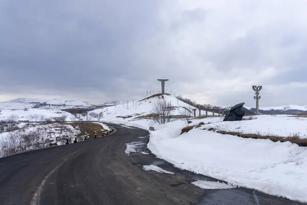 stock image Didgori battle memorial, Georgia. Winter and snow, overcast. Giant swords stuck in the ground. Monument on the hill. Asphalt road leading to the mountain.