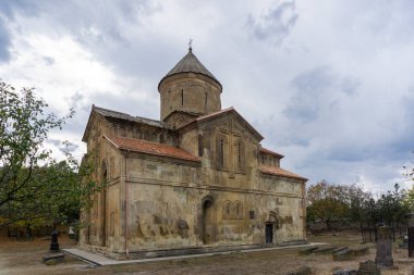 Avlu ve Ertatsminda kilisesinin sonbahar manzarası. Renkli ağaçlar, yapraklar ve çimenler. Kilisenin duvarlarında güzel levrekler var. Tepede haç var. Georgi.