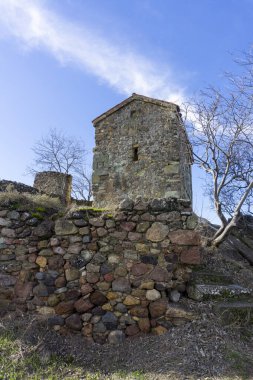 Ortaçağ kalesinin içinde bir kayanın üzerinde. Küçük taş kilise. Renkli taşlardan bir duvar. Bulutlu parlak mavi gökyüzü. Kveshi kalesi. Georgia