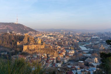 Şehirde gün doğumu. Narikala kalesi, cami, Metekhi kilisesi, TV kulesi, Mtkvari nehri. Tiflis, Gürcistan