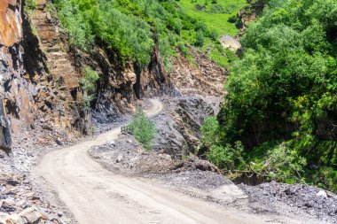 Uçurumla vadi arasında tehlikeli bir dağ yolu var. Küçük tahta bir köprü. Kayalar, ağaçlar, çalılıklar