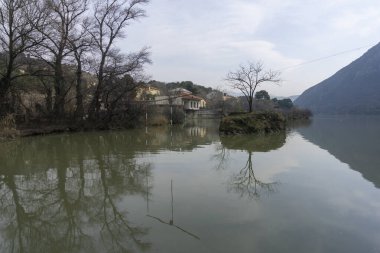 Mtskheta kentindeki kıyıdan Mtkvari (Kura) nehrinin manzarası. Gökyüzünün yansıması, sudaki binalar ve ağaçlar.