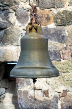 Paslı bir zincire asılı eski pirinç bir çan. Arkaplanda bulanık taş duvar