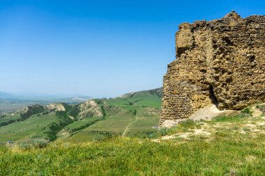 Eski Ksani kalesinin taş duvarı kısmen yıkıldı. Dağ manzarası. Yeşil çimen.