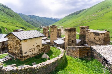 Delikleri ve küçük kilisesi olan taş kuleler. Arka planda yeşil dağlar ve bulutlu gökyüzü. Ushguli köyünün kale kuleleri ve caddeleri.