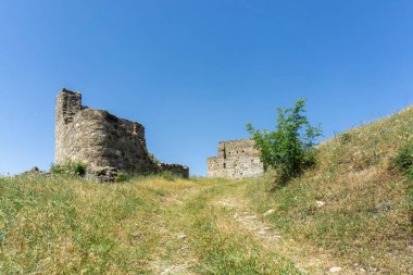 Toprak bir yol tepedeki ortaçağ kalesinin kalıntılarına çıkar. Taş duvar ve eski bina görülebilir. Mavi parlak gökyüzü. Manavi, Georgia.
