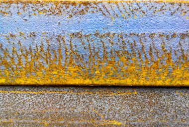 Üzerinde çizikler ve turuncu lekeler olan paslı demir levha. Mavi, kahverengi, cyan ve sarı renkler
