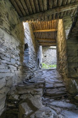 Taş duvarlı tünel geçidi ve kütüklerle kaplı bir tavan. Ortaçağ köyü Shatili sokakları.