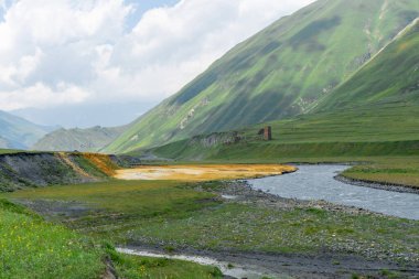 A stream of brown, yellow and white colored mineral water flows into the Terek River clipart