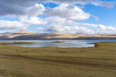 Curved shores of Lake Paravani in front of mountains covered with clouds clipart