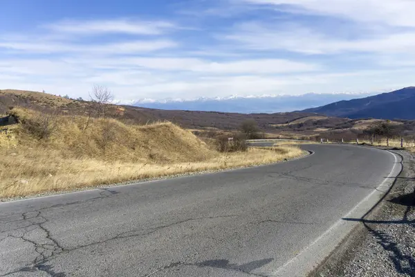 Gombori geçidinden kar kaplı Kafkasya bayırı manzarası. Asfalt yol, sarı çimen, parlak gökyüzü