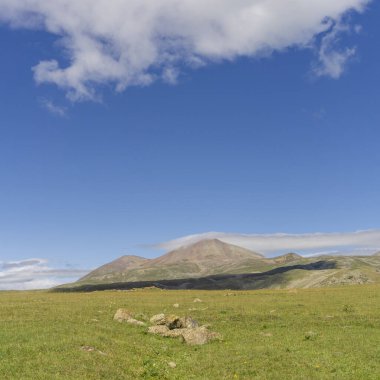 Büyük ve küçük dağlar Abuli bulutlarla kaplı. Önünde taşlar olan yeşil alan.