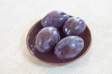 Dört koyu mor eriğin üst görüntüsü. Kahverengi bir tabakta, açık bir masada su damlaları.