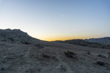 Dağlarda güneş doğmadan önce. Gökyüzünün turuncu parçası. Mavide parlak ay