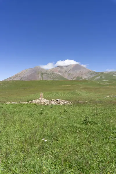 stock image Small and big mountains of Abuli covered with cloud. A marker for tourists in the form of a tall stone on a green field surrounded by a pile of stones.