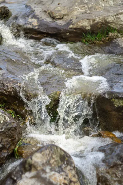 stock image A close view of a waterfall cascading onto the rocks. Water splashes, dry leaves and foam are visible