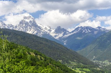 Dağlardaki vadi manzarası ağaçlar ve çalılarla çevrili. Ushba Dağı 'nın karlı zirvesinin üzerindeki bulutlar