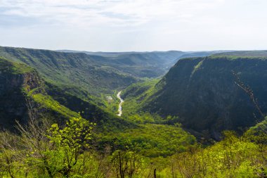 Dipteki nehir, ağaçlar ve çalılarla kaplı kayalarla çevrili derin bir kanyondur. Bulutlu mavi gökyüzü