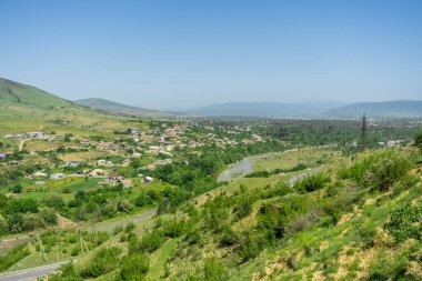 Nehir boyunca uzanan Ksani Nehri 'nin üzerinden, çim ve çalılarla kaplı düzlüklere bakın. Arka planda dağlar ve mavi gökyüzü