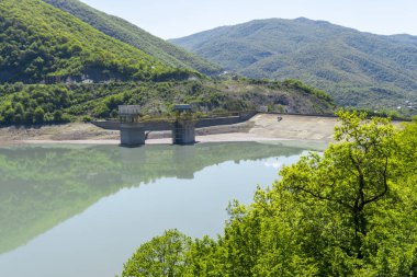 Zhinvali Barajı Aragvi Nehri üzerinde bir hidroelektrik barajıdır. Yeşil çimenler, mavi gökyüzü, arka planda dağlar.