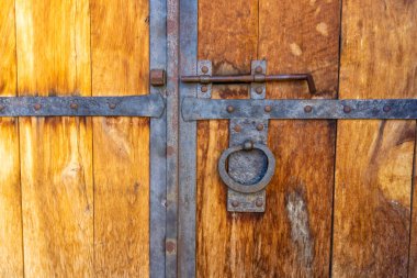 Demir kravatlarla kaplı eski ahşap bir kapının detayları, bir tokmak, paslı bir cıvata. Tahtanın yapısı görülebilir..