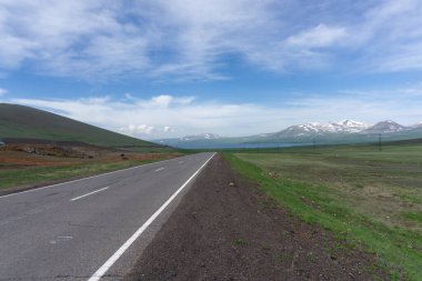 Paravani gölü ve dağlarına giden yol. Doğal göl, mavi su, bulutlar, karlı dağlar ve mavi gökyüzü. Gürcistan 'da