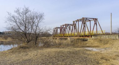 Eski demiryolu köprüsünün yan görüntüsü. Gölün bir kısmı görülebilir. Açık mavi gökyüzü