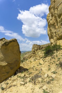Sarı kayalar arasında geçiş. Parlak mavi gökyüzü ve arka planda bulutlar.