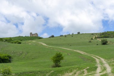 Skhvilo kalesiyle tepeye çıkan toprak yol. Yeşil çimen, bulutlu gökyüzü