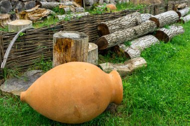 Çimlerin üzerindeki küçük Kvevri Qvevri Churi - Geleneksel Gürcistan şarabının mayalanması, depolanması ve yaşlanmasında kullanılan toprak kapları. Kuru kütükler ve arka planda bir çit.