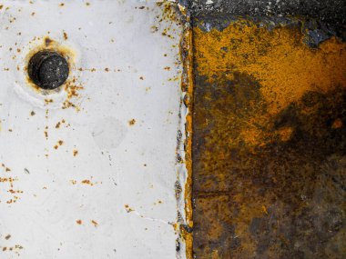 İki eski metal plaka kaynaşmış. Biri kahverengi pasla kaplanmış, diğeri beyaz boyanmış ve cıvata deliği var..