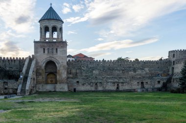 Svetitskhoveli Katedral avlusunun kale duvarı. Taş merdivenli çan kulesi. Kapılı kemerli geçit. Bulutlu parlak gökyüzü