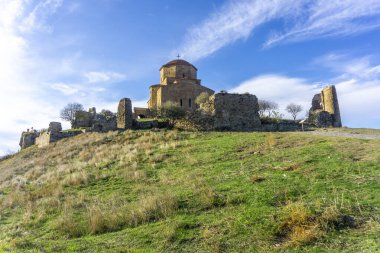 Tepedeki Jvari Manastırı. Kulenin yıkıntıları ve kale duvarı. Yeşil çimen, parlak mavi gökyüzü